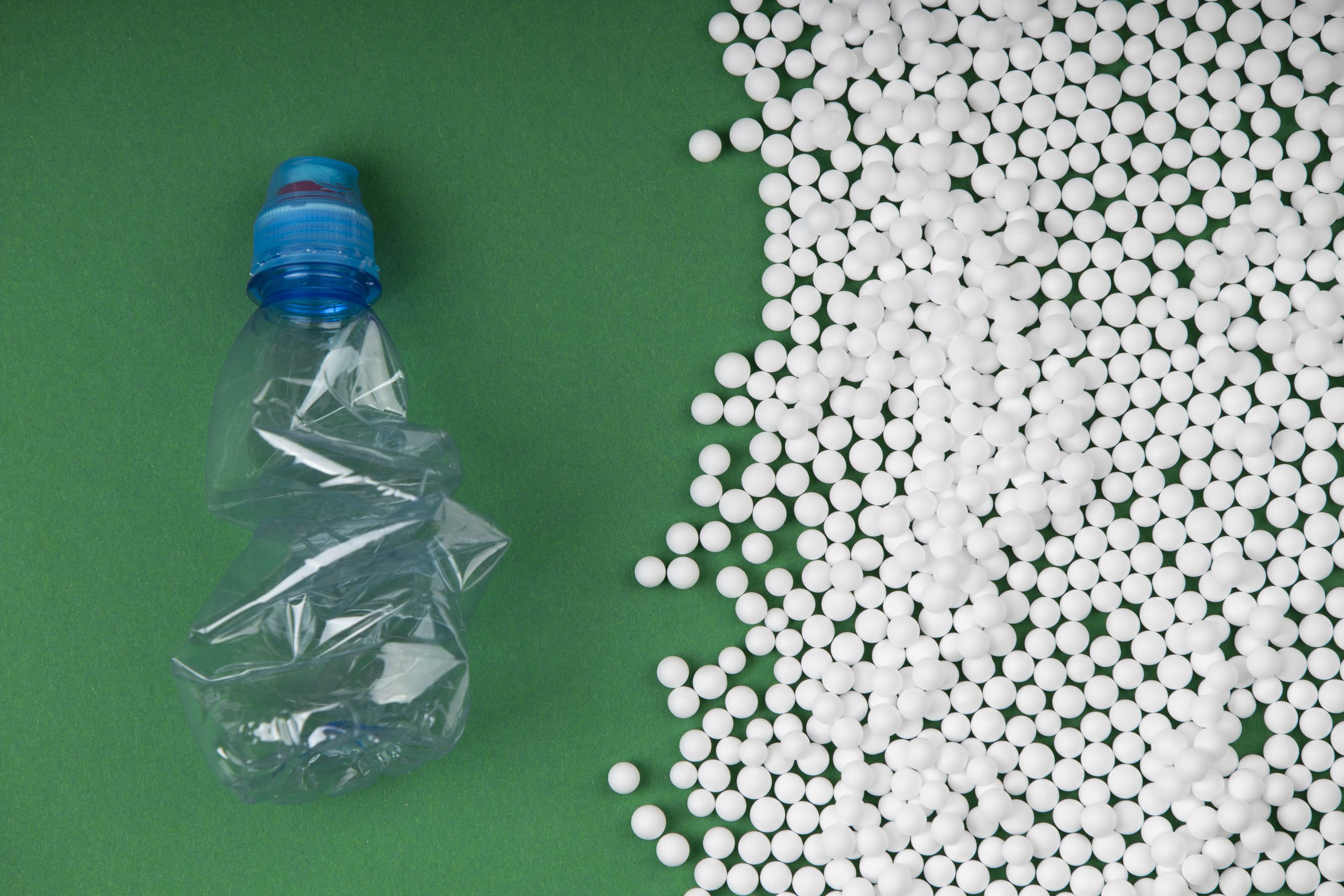 Granulat tworzywa PA11 poliamid obok zgniecionej plastikowej butelki na zielonym tle, symbolizujący recykling i zrównoważoną produkcję.