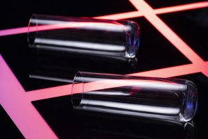 Dwa przezroczyste cylindry na tle z czerwonymi liniami, prezentujące efekt gładkiej powierzchni uzyskany dzięki powłokom fluoropolimerowym.