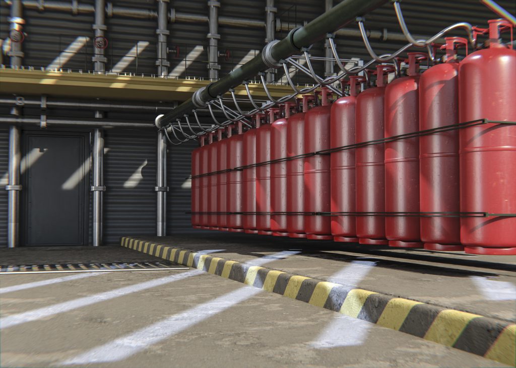 Rząd czerwonych butli z gazem gaśniczym podłączonych do kolektora w hali przemysłowej, stanowiący element stałej instalacji gaśniczej. To przykład gazowego systemu przeciwpożarowego.