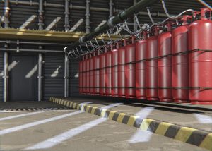 Rząd czerwonych butli z gazem gaśniczym podłączonych do kolektora w hali przemysłowej, stanowiący element stałej instalacji gaśniczej. To przykład gazowego systemu przeciwpożarowego.