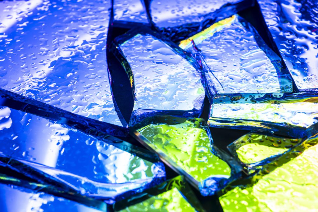 Krople wody na popękanym, kolorowym szkle. Obraz doskonale ilustruje hydrofobowość, czyli właściwość odpychania wody, którą zapewniają powłoki fluoropolimerowe.