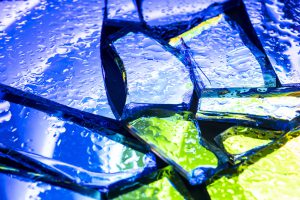 Krople wody na popękanym, kolorowym szkle. Obraz doskonale ilustruje hydrofobowość, czyli właściwość odpychania wody, którą zapewniają powłoki fluoropolimerowe.