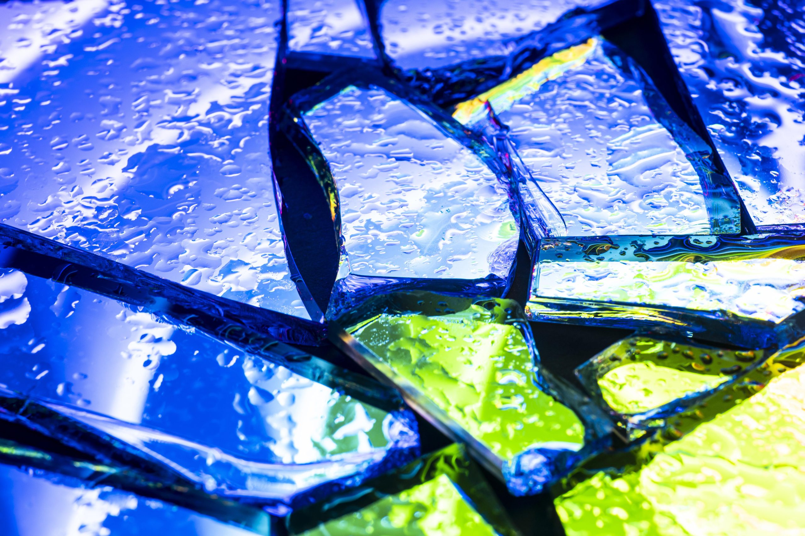 Krople wody na popękanym, kolorowym szkle. Obraz doskonale ilustruje hydrofobowość, czyli właściwość odpychania wody, którą zapewniają powłoki fluoropolimerowe.